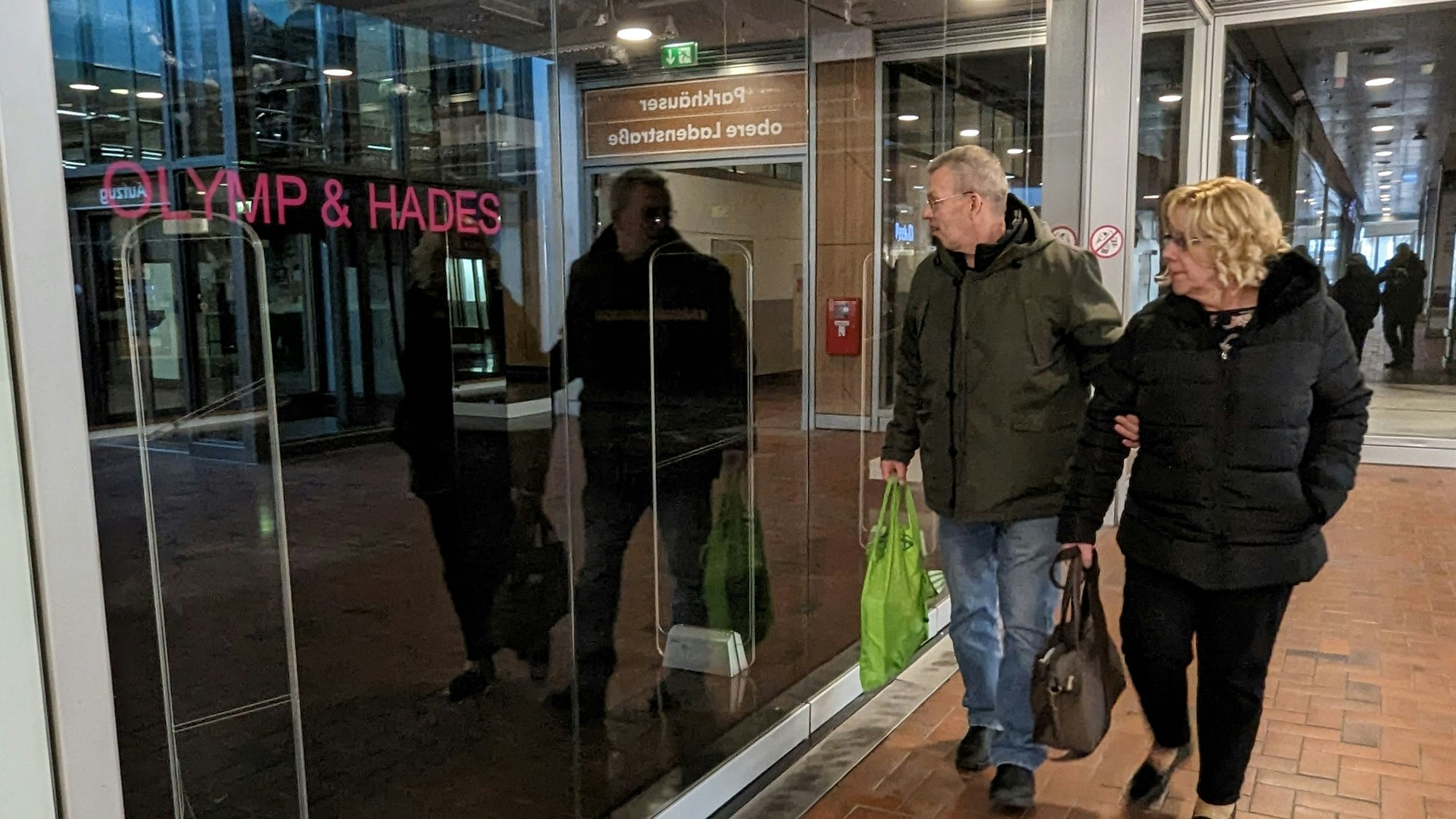 Das Foto zeigt zwei Passanten vor dem leerstehenden Ladenlokal des Textilhändlers Olymp & Hades.