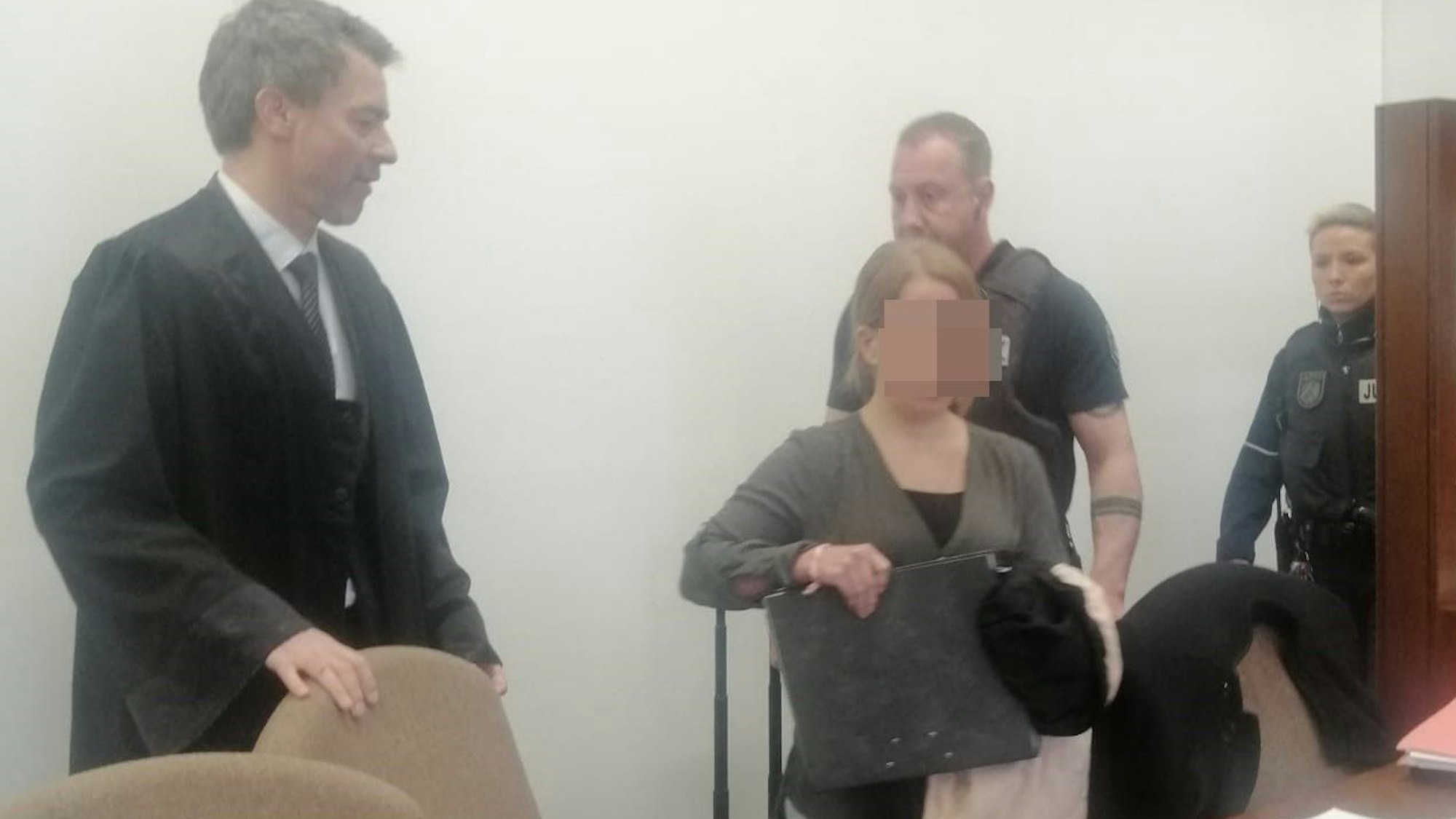 Das Foto zeigt die Angeklagte im Gerichtssaal. Zu sehen sind zudem ihr Verteidiger und zwei Justizvollzugsbeamte.