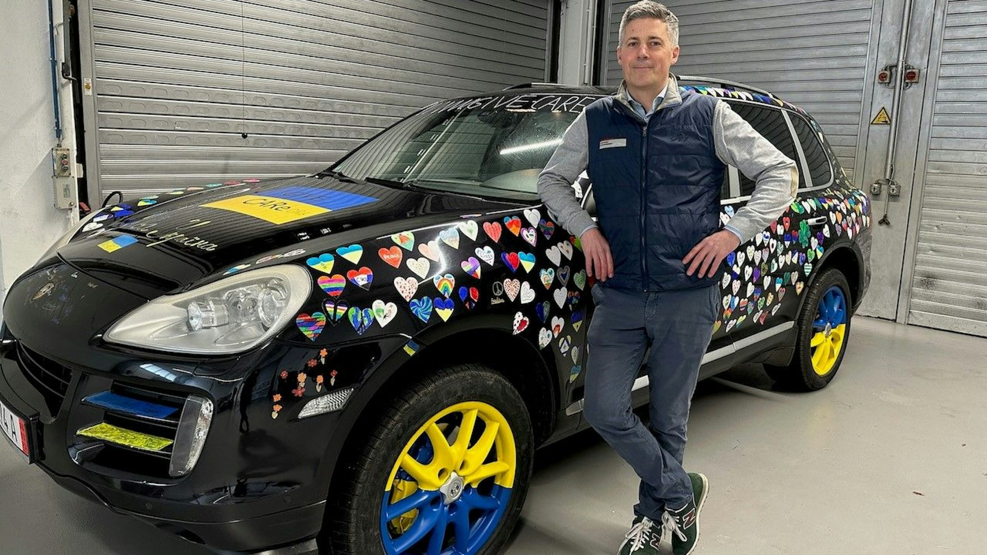 Ein Mann steht vor seinem mit Aufklebern beklebten Porsche.