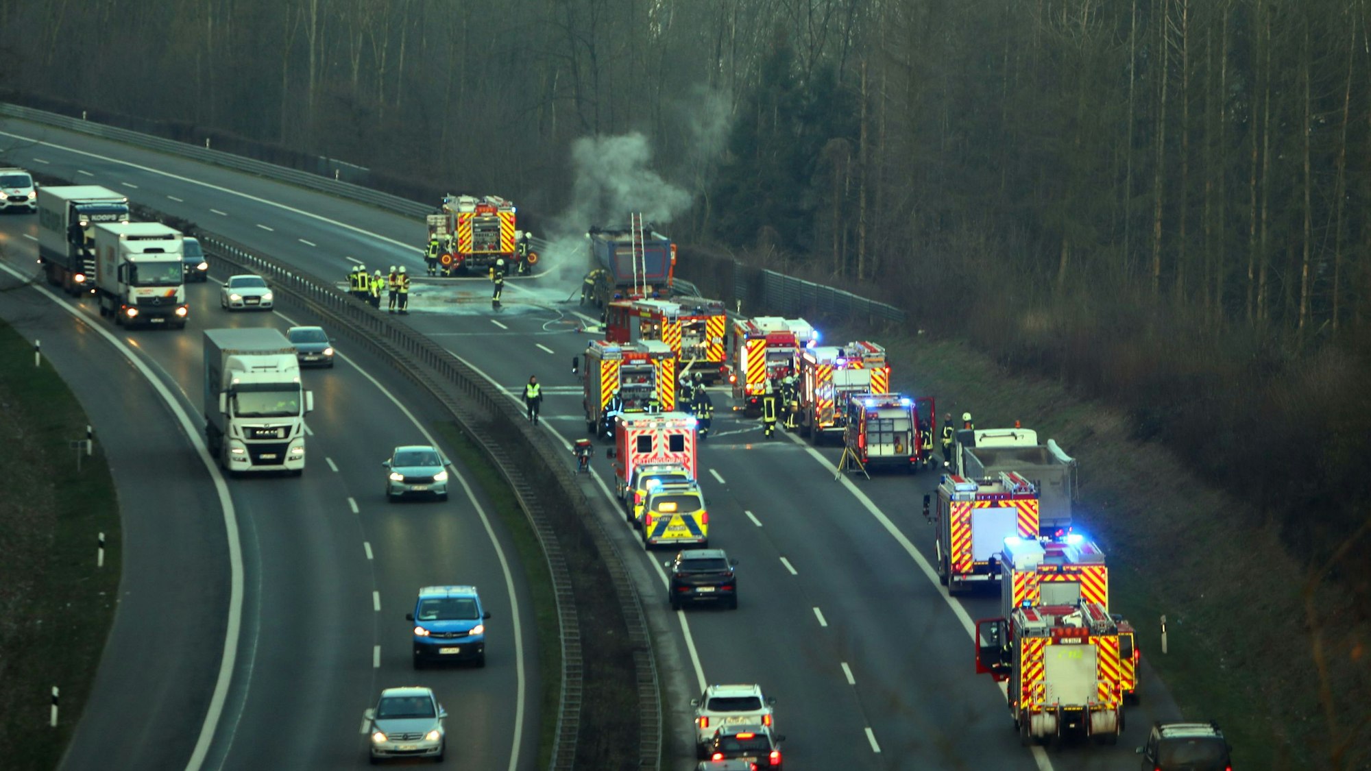 Feuerwehrautos stehen auf der gesperrten Autobahn, Feuerwehrleute löschen einen Lastwagen aus dem noch Rauchschwaden aufsteigen.