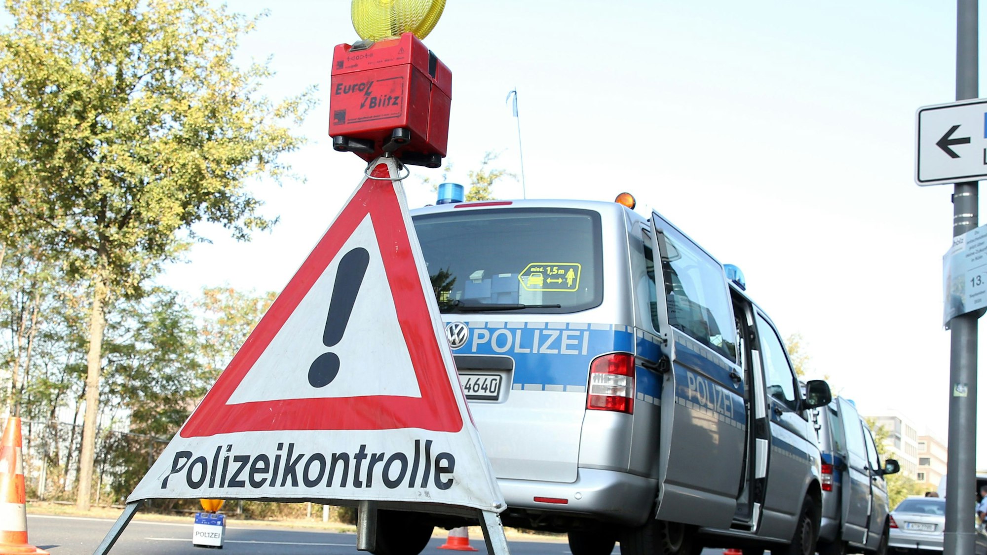 Ein Polizeiwagen steht am Straßenrand, davor ein Warndreieck mit der Aufschrift „Polizeikontrolle“.