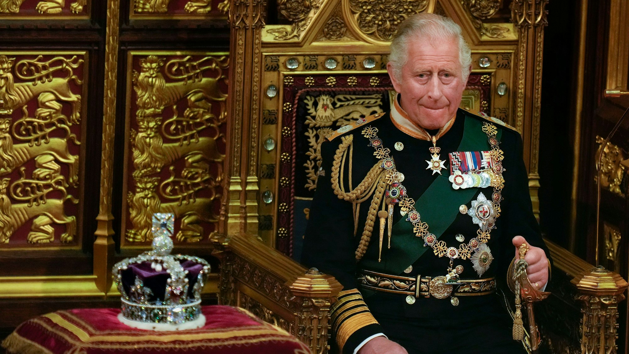 König Charles III. auf dem Thron. Neben ihm die Krone.