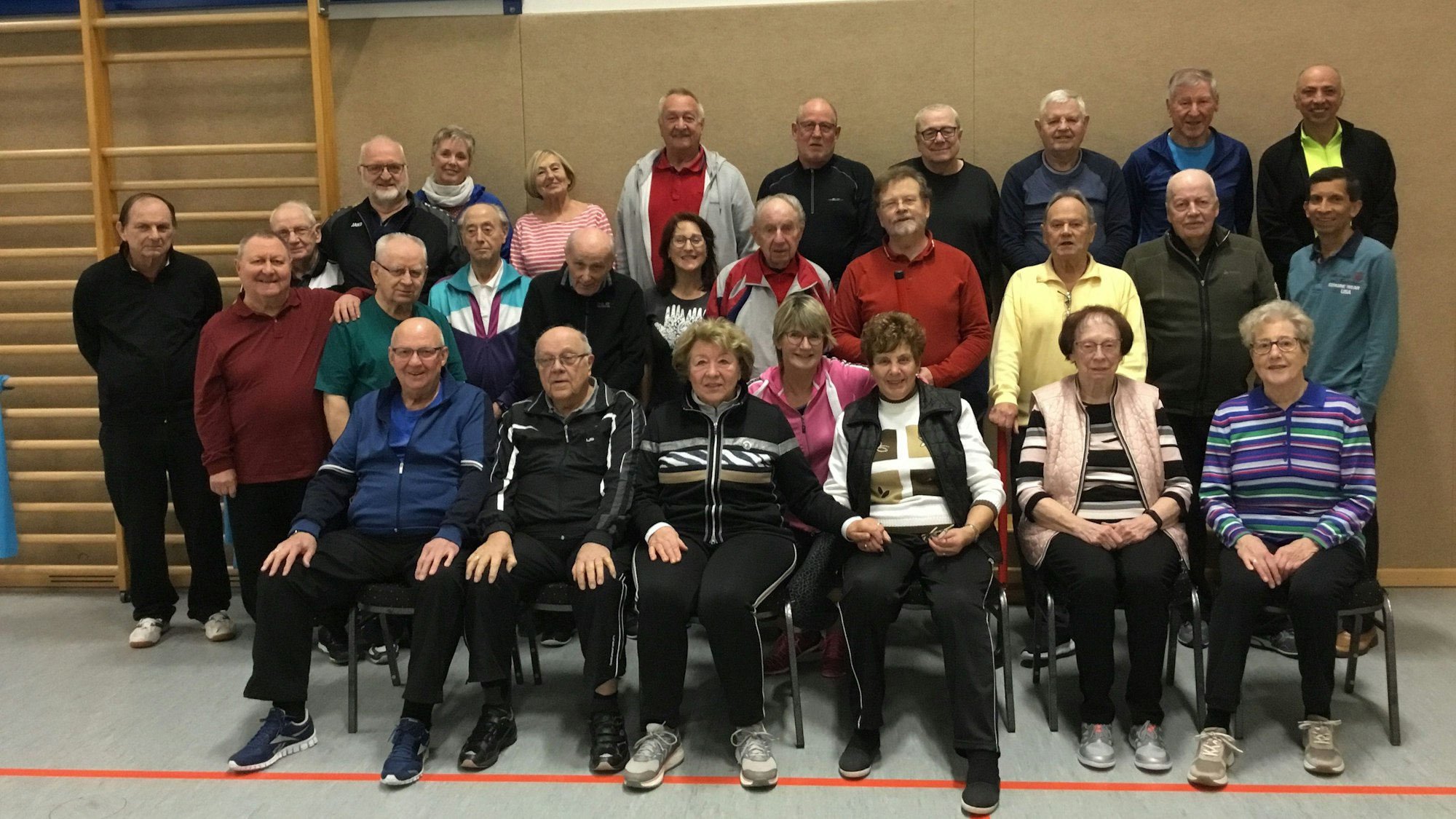Die Herzsportgruppen mit ihren Trainerinnen steht vor der Wand einer Turnhalle.