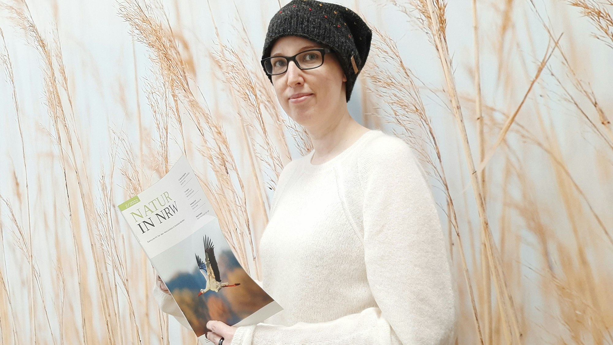 Sabine Grützmacher trägt eine Mütze auf dem Kopf. In den Händen hält sie ein Magazin mit dem Titel „Natur in NRW“.