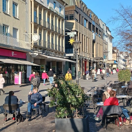 Eine Fußgängerzone im Sonnenlicht, Menschen sitzen im Straßencafé.