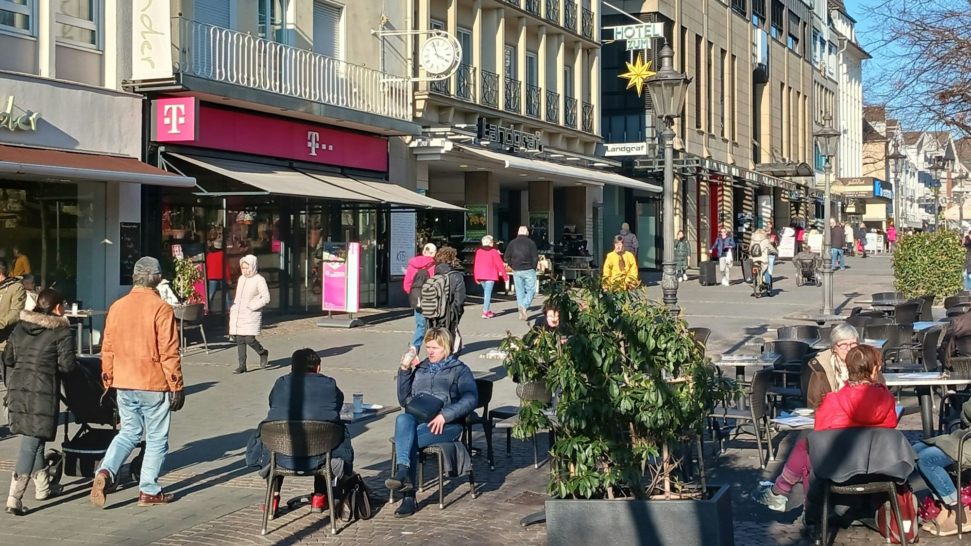 Eine Fußgängerzone im Sonnenlicht, Menschen sitzen im Straßencafé.