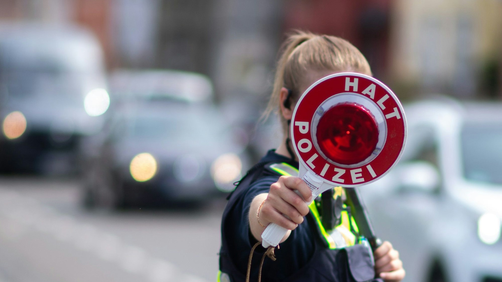 Eine Polizistin steht auf einer Straße und hält eine Anhaltekelle hoch.