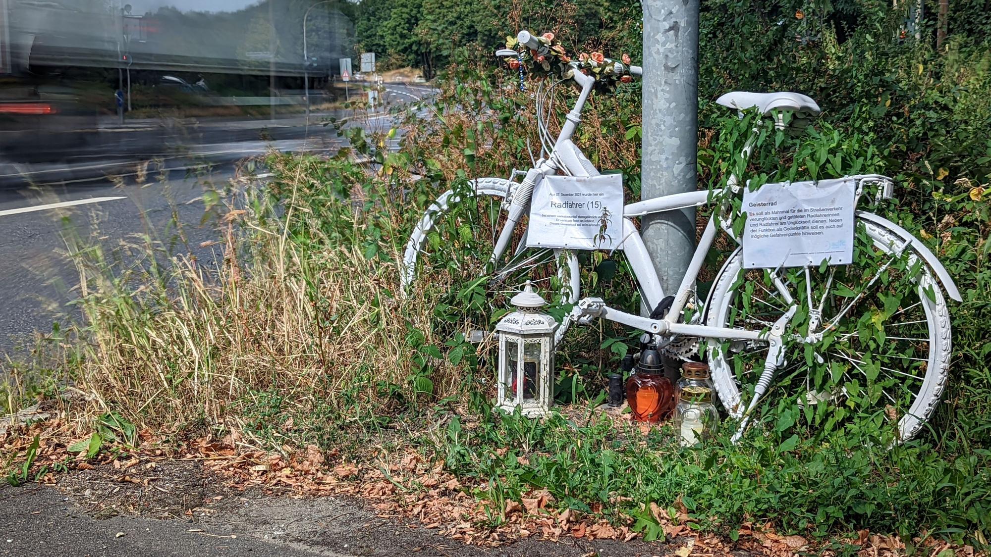 Das Foto zeigt ein symbolisches Geisterrad an der Frechener Straße vor der Kreuzung Sudetenstraße erinnert an den 15-jährigen Radfahrer, der dort im Dezember 2021 von einem abbiegenden Lkw überrollt und getötet wurde.