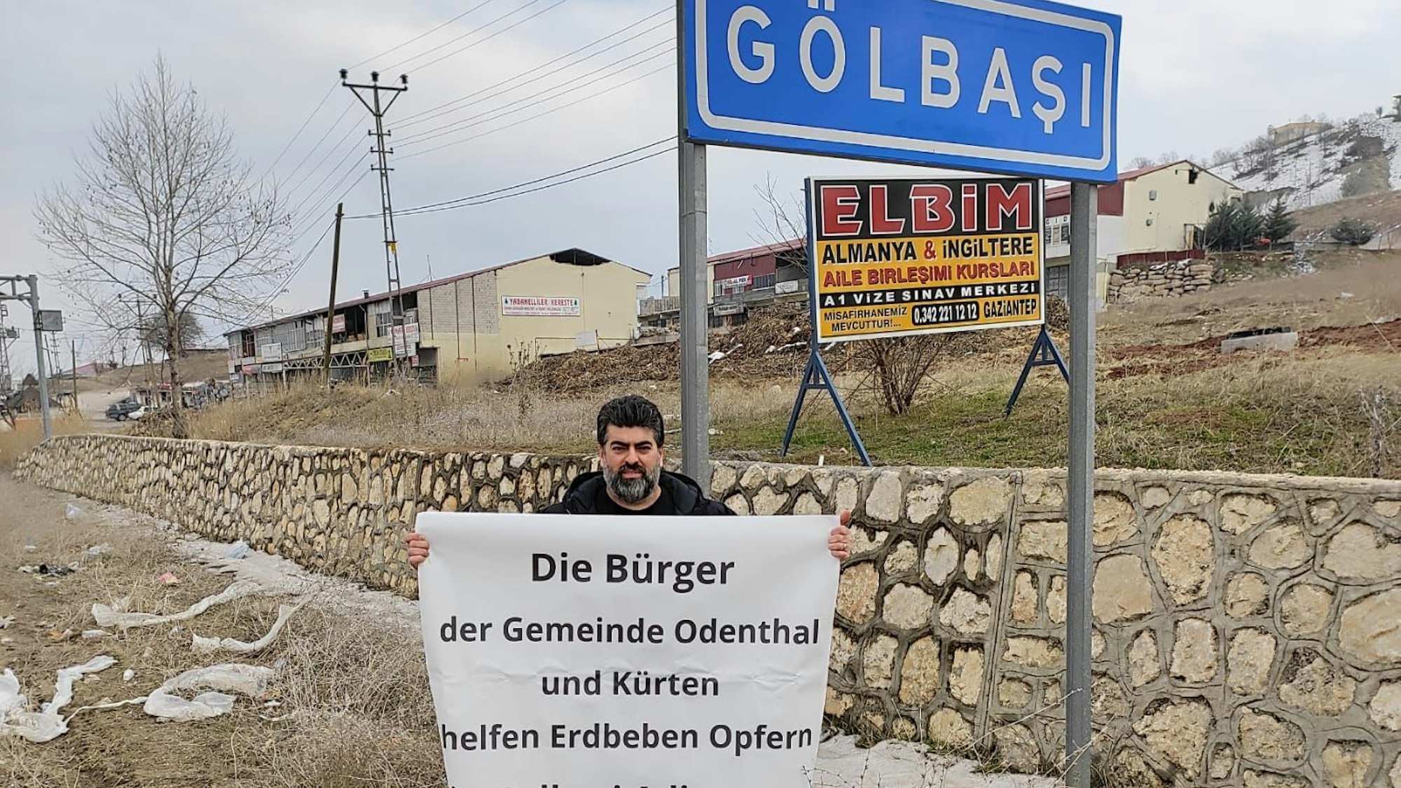 Erkan Karahan steht mit einem Banner unter dem Ortsschild von Golbasi.