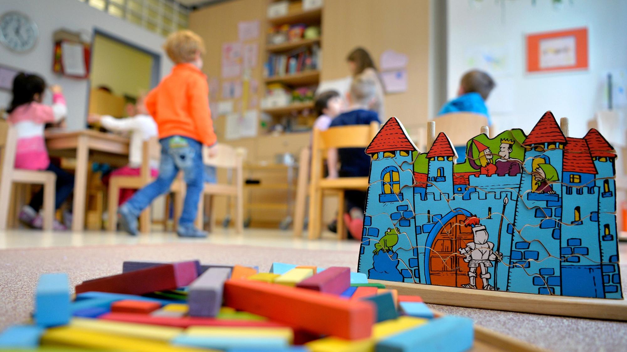 Kinder spielen in einer Kindestagesstätte, im Vordergrund liegt Spielzeug auf dem Boden.