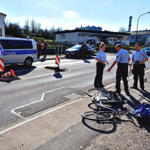 Polizisten stehen auf einer Straße, ein Rad liegt auf dem Boden.