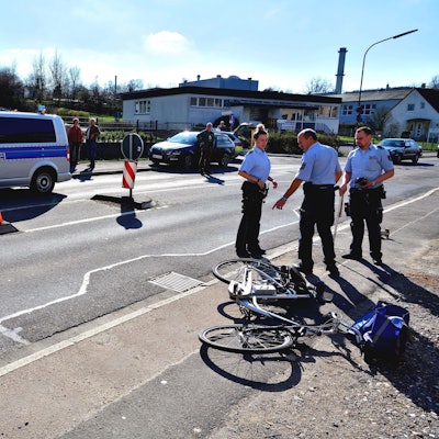 Polizisten stehen auf einer Straße, ein Rad liegt auf dem Boden.