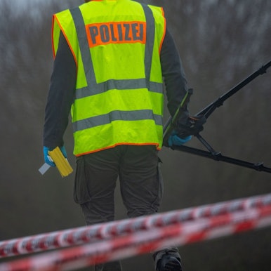 Ein Polizist untersucht einen Tatort. Er trägt eine gelbe Polizei-Weste. (Symbolbild)