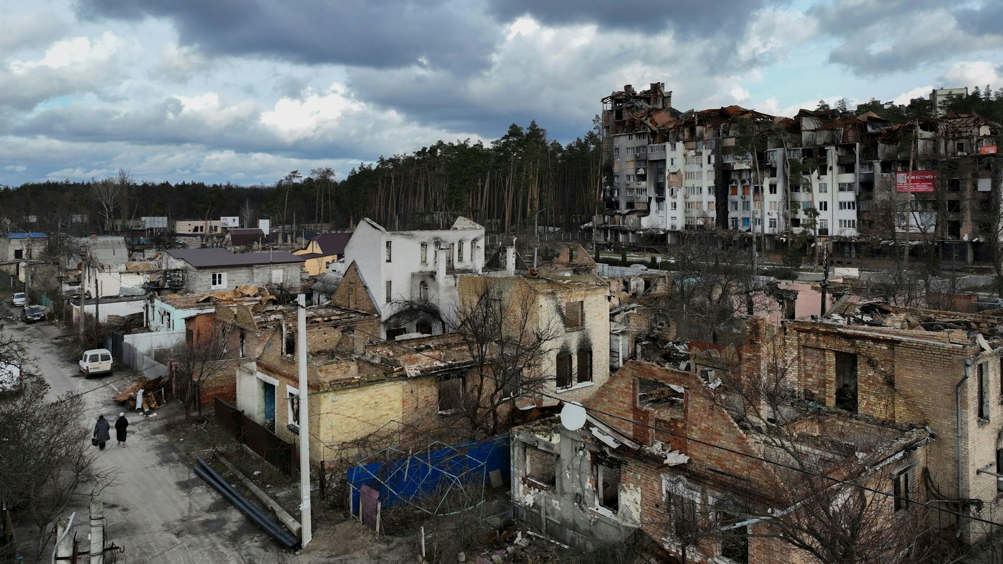 Frauen gehen zwischen zerstörten Gebäuden entlang.