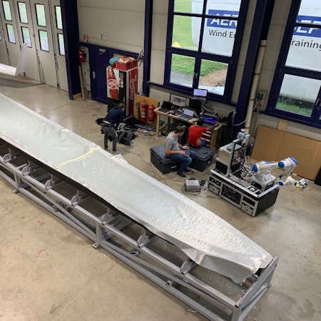 Bei der Aeroconcept GmbH ist für einen Test ein Faserpaket für eine Rotorblattspitze ausgelegt worden. Techniker sitzen neben der Form in einer Flugzeughalle.