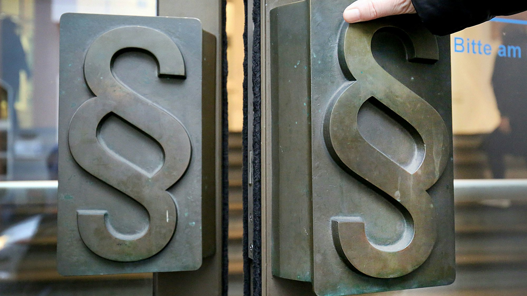 Man sieht die Hand einer Person, die die Türe zum Landgericht auszieht.