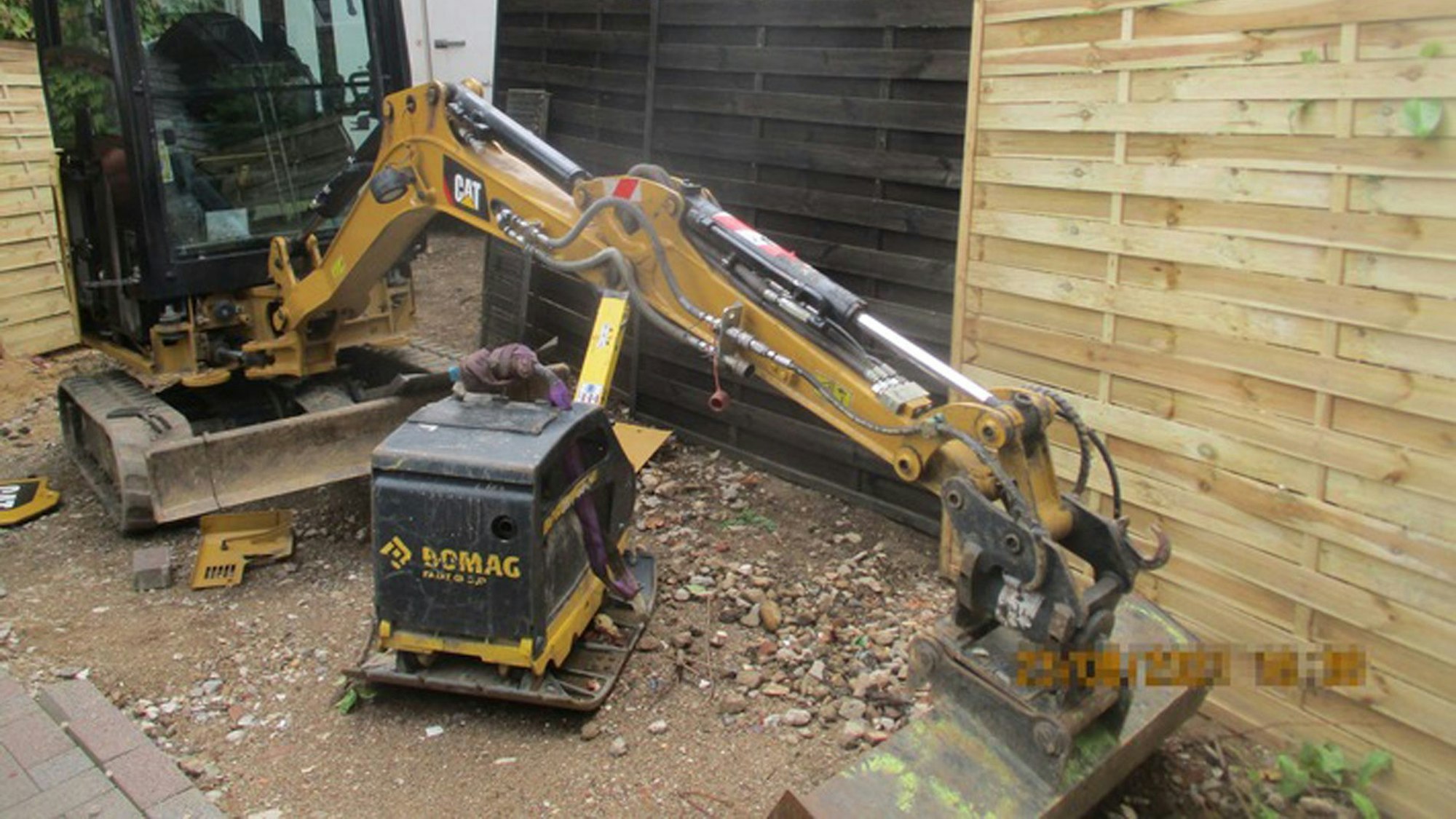 Eine Rüttelplatte und ein Bagger auf einer Baustelle.