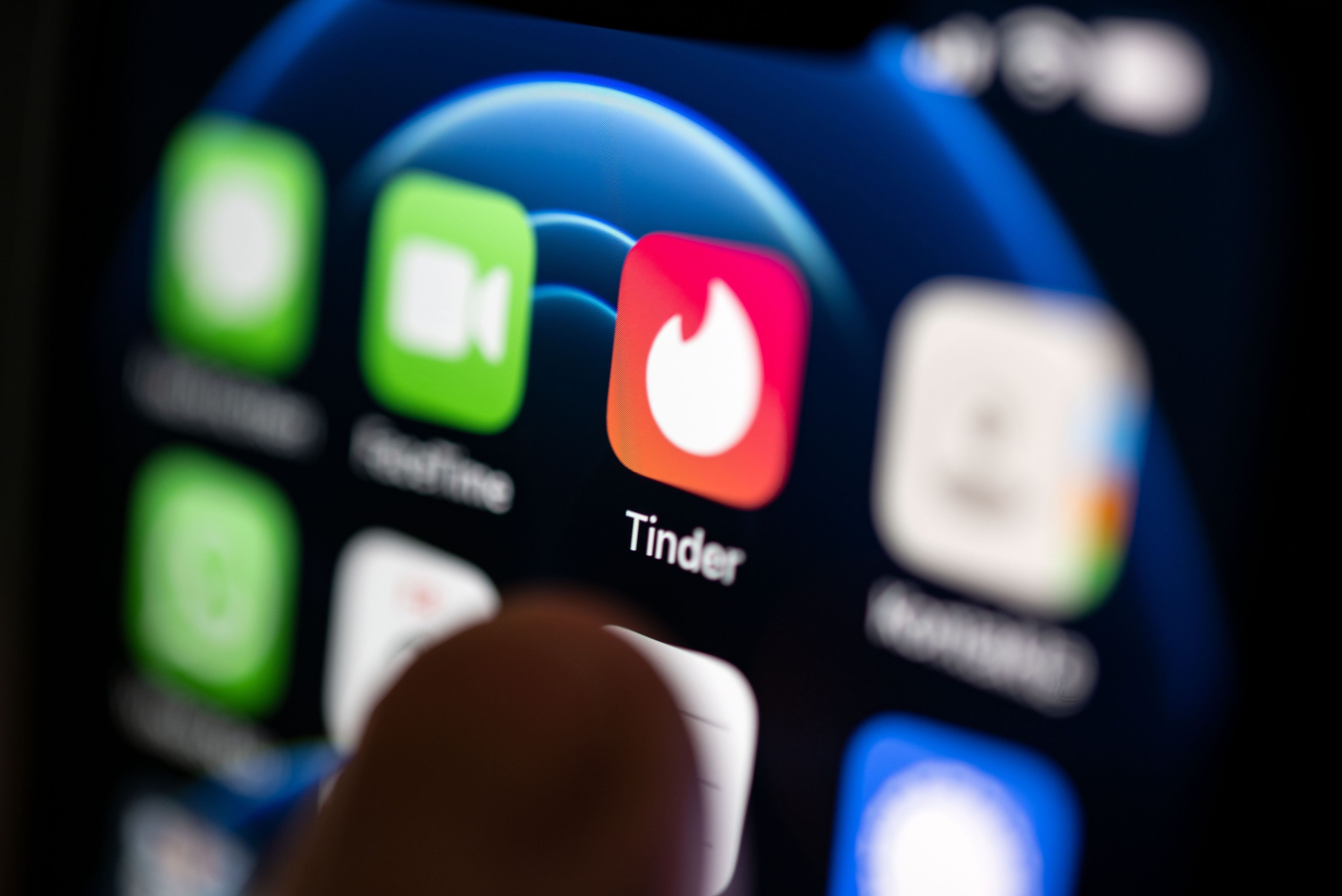 Ein Finger bedient ein Smartphone, auf dem unter anderen die App von Tinder installiert ist.