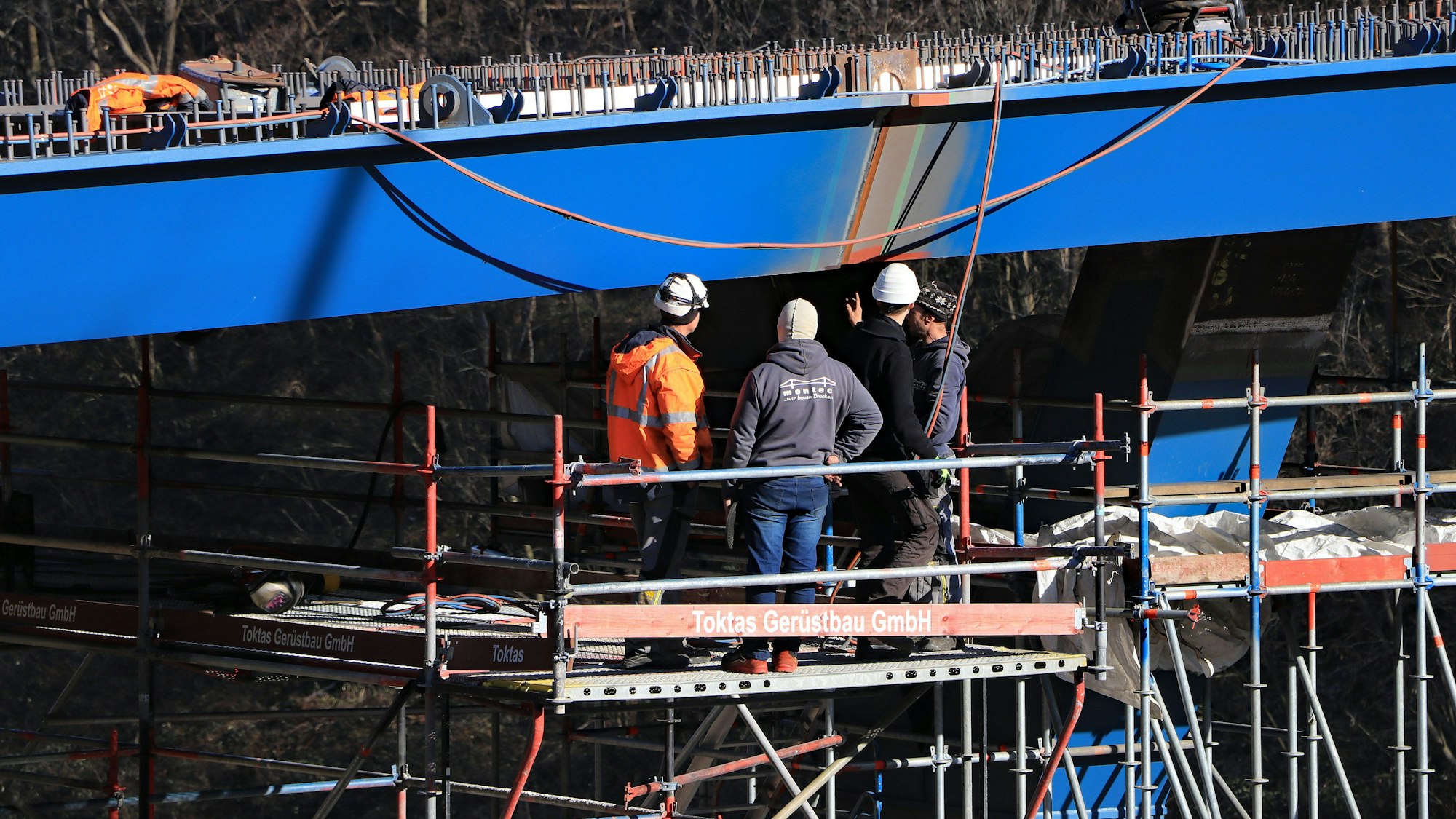 Das Foto zeigt, wie Ingenieure auf einem Gerüst stehend in schwindelerregender Höhe die Brückenteile kontrollieren.