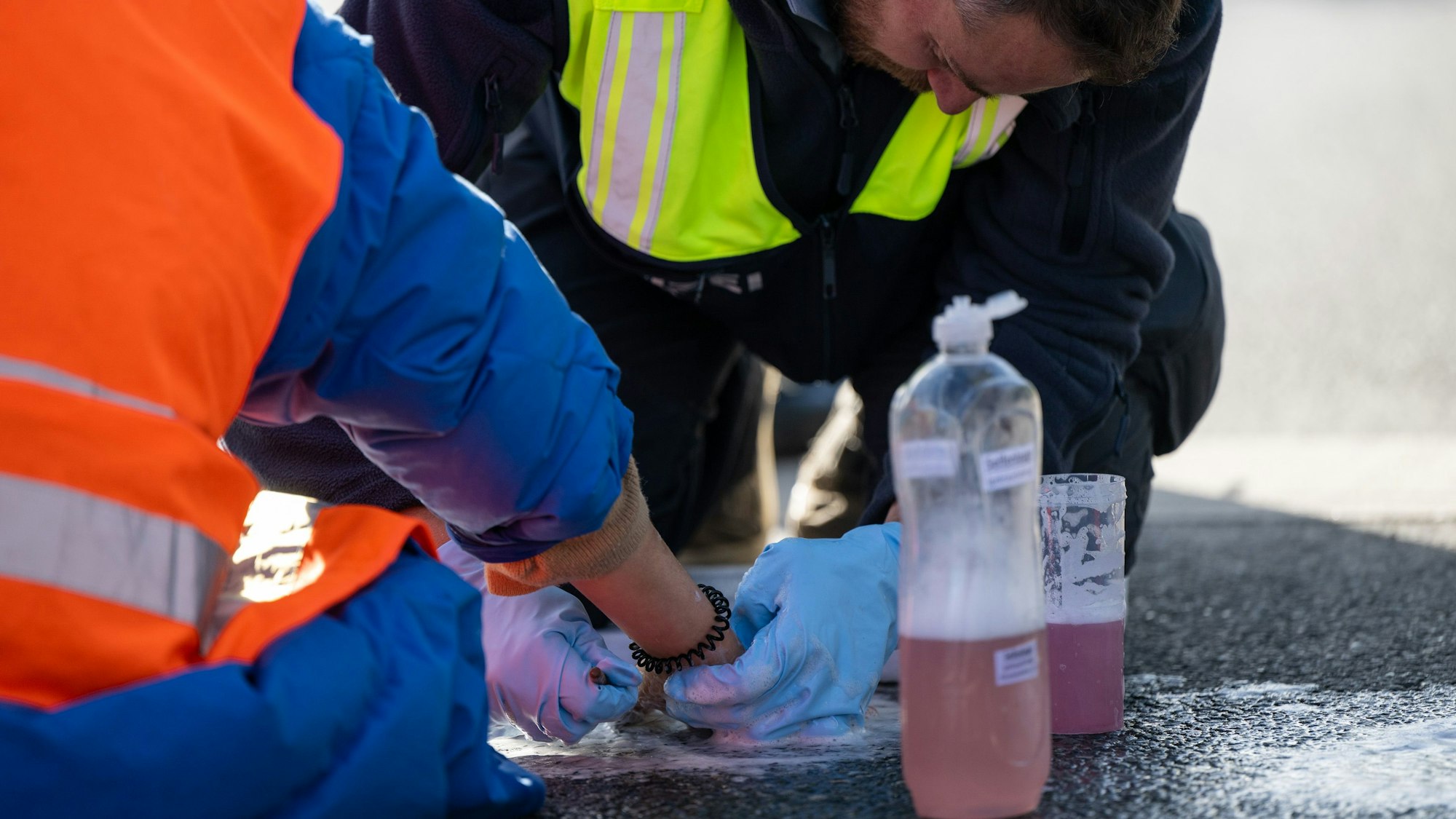 Ein Polizist löst die festgeklebte Hand eines Klimaaktivisten, der sich zuvor auf eine Straße geklebt hat.