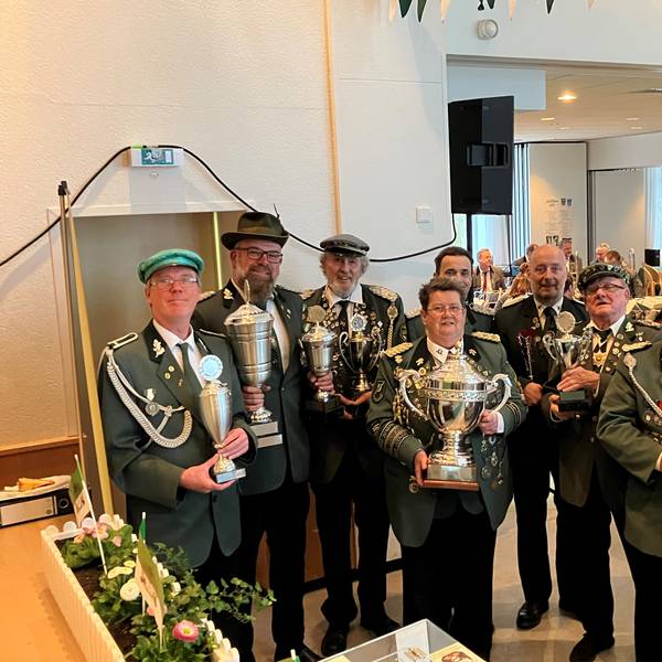 Mehrere Männer in Schützenuniform stehen in einer Reihe. In den Händen halten sie Pokale.