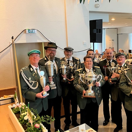 Mehrere Männer in Schützenuniform stehen in einer Reihe. In den Händen halten sie Pokale.