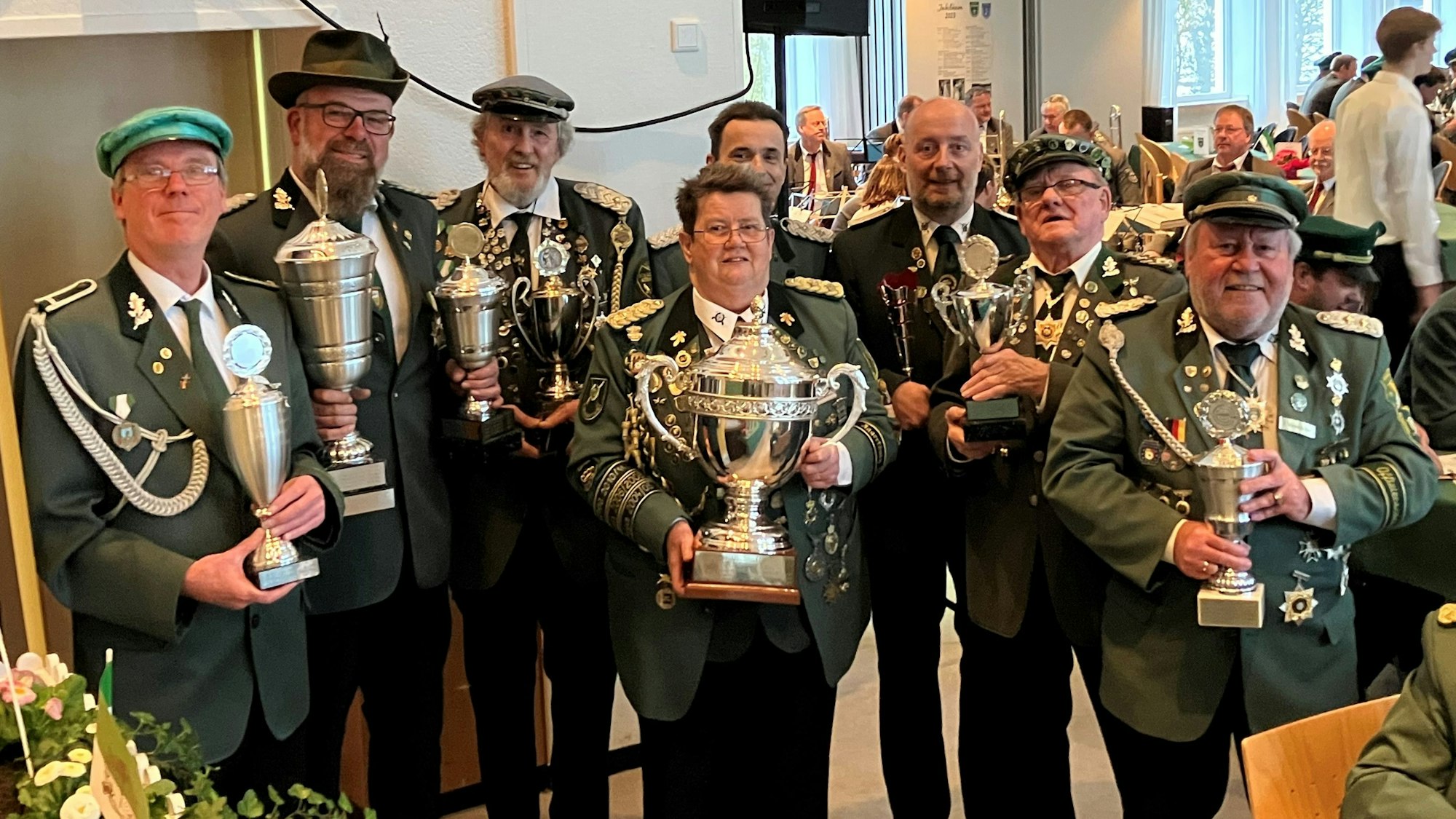 Mehrere Männer in Schützenuniform stehen in einer Reihe. In den Händen halten sie Pokale.