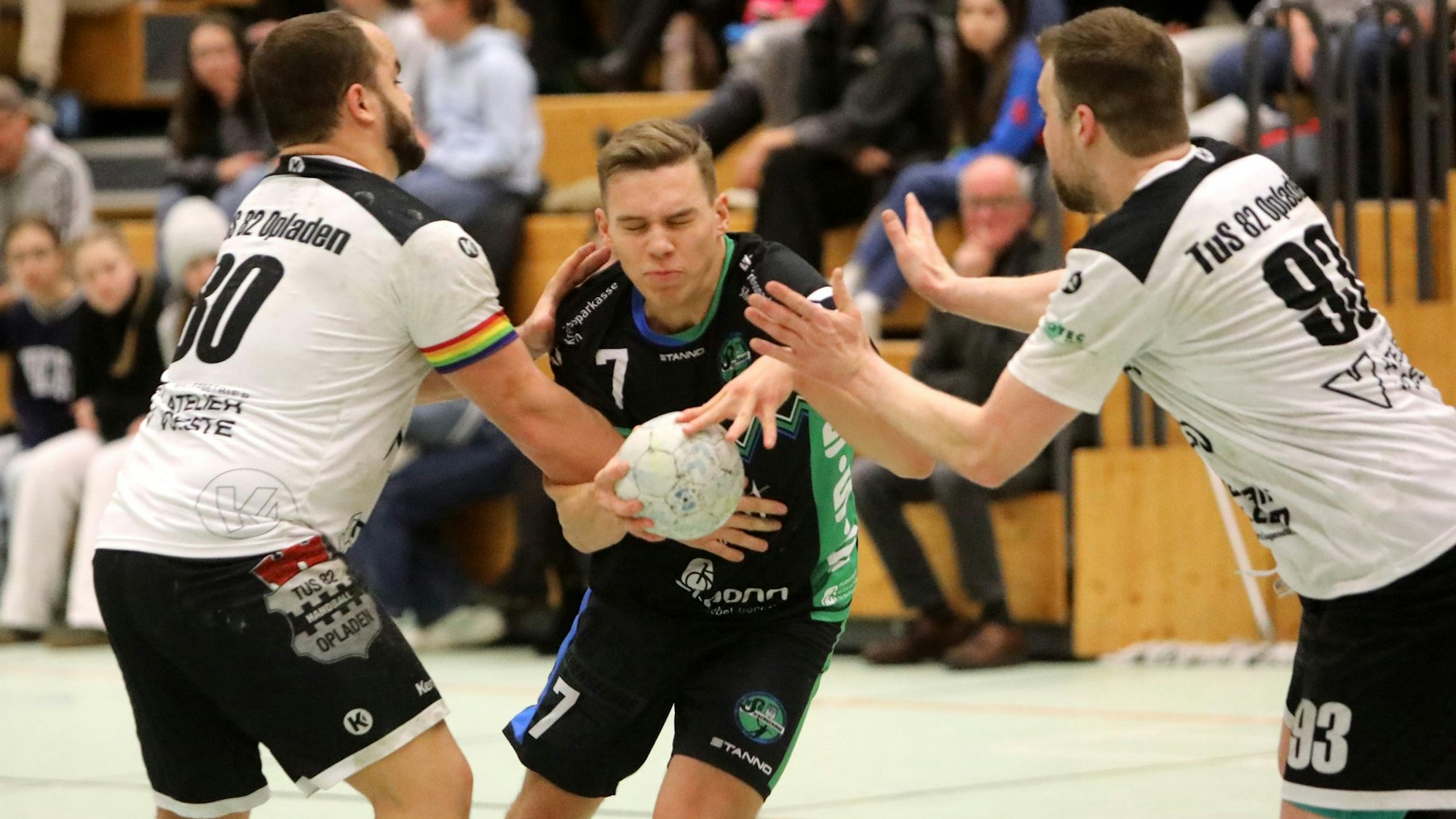 David Runge (Mitte) von der HSG Siebengebirge schließt die Augen und hält den Ball fest, während ihn zwei Opladener Gegenspieler in die Zange nehmen und attackieren.