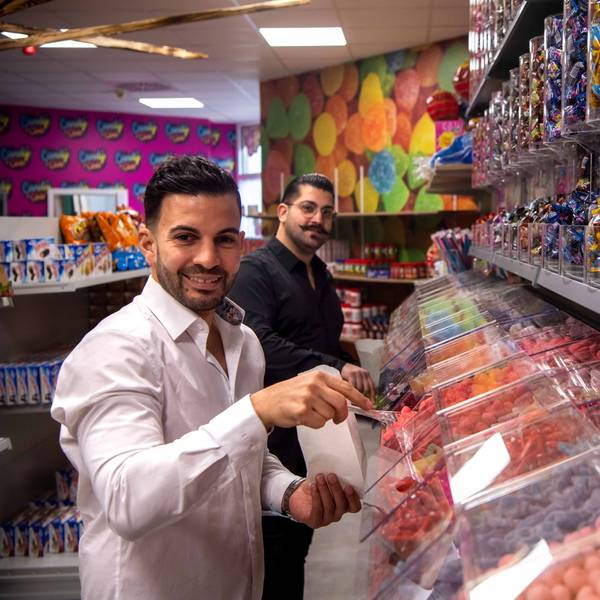 Die Betreiber des Candy Shop in Euskirchen stehen vor der Süßigkeitenwand.