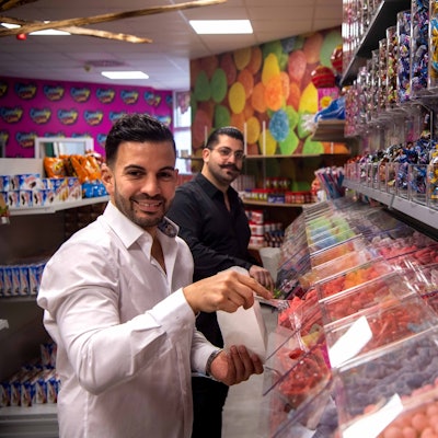 Die Betreiber des Candy Shop in Euskirchen stehen vor der Süßigkeitenwand.