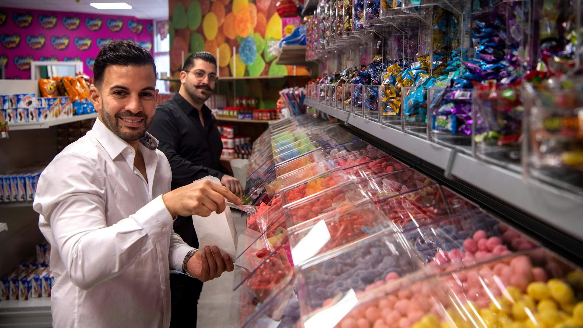 Die Betreiber des Candy Shop in Euskirchen stehen vor der Süßigkeitenwand.