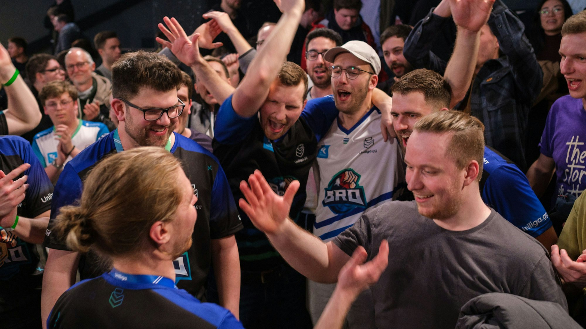 Viele junge Männer in T-Shirts jubeln und klatschen sich gegenseitig ab.