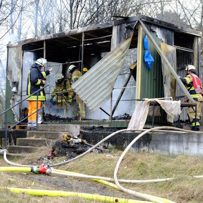 Man sieht Einsatzkräfte, wie sie die letzten Brandherde im Container löschen.