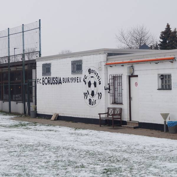 Der Rasen ist mit Schnee bedeckt, dahinter steht ein einstöckiges Vereinsheim mit der Aufschrift „FC Borussia Buir“.