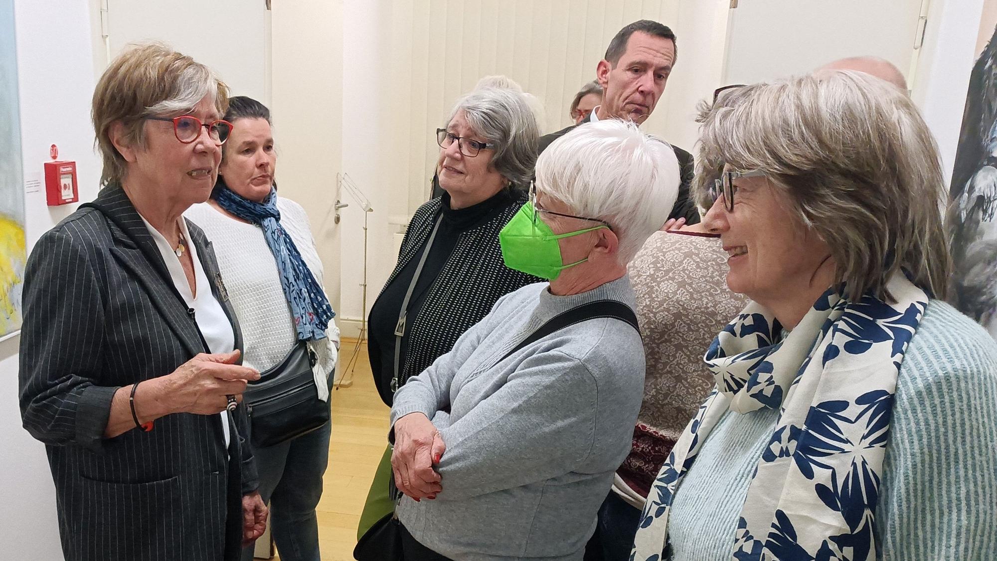 Die Künstlerin Gerda Laufenberg steht links und spricht angeregt mit Besuchern.