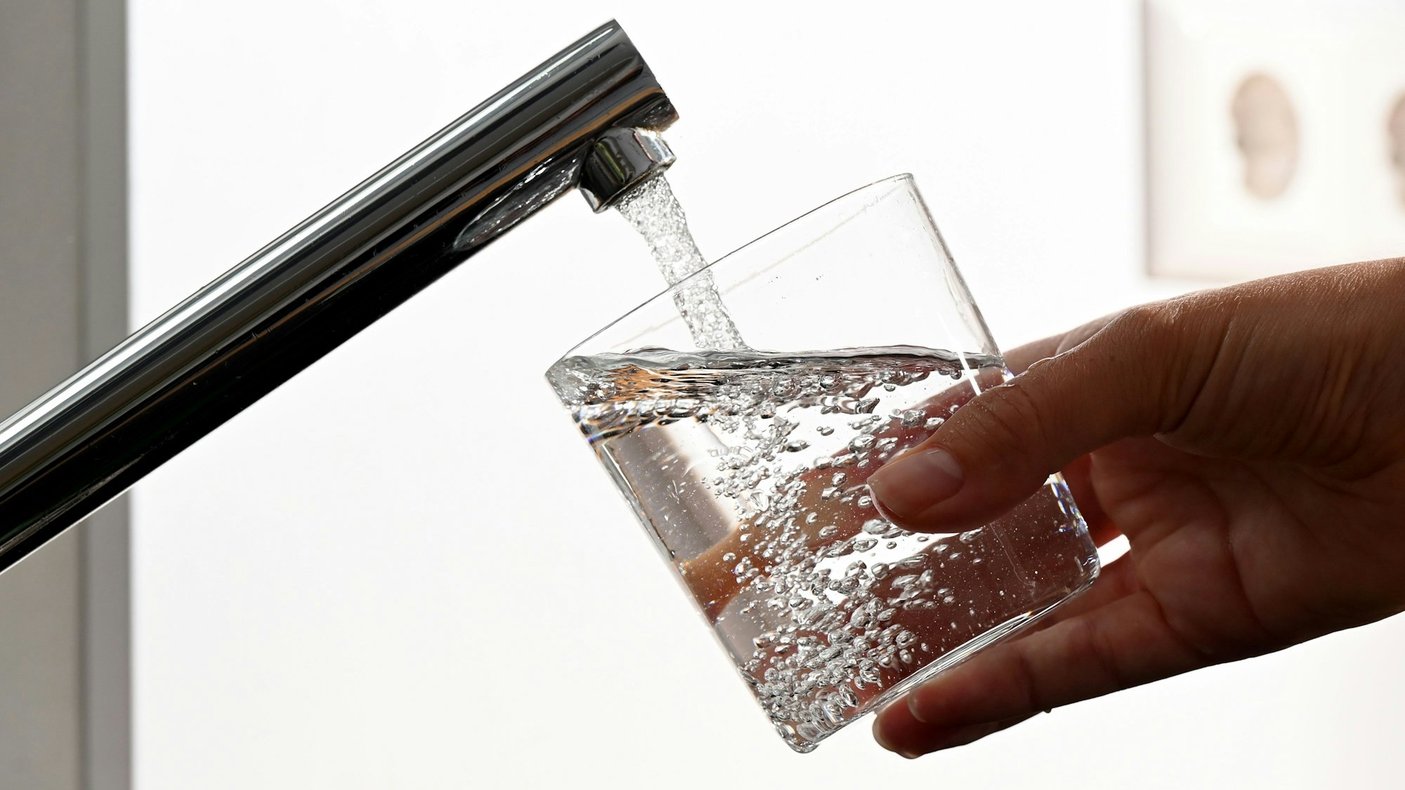 Eine Hand hält ein Wasserglas unter einen Wasserhahn.