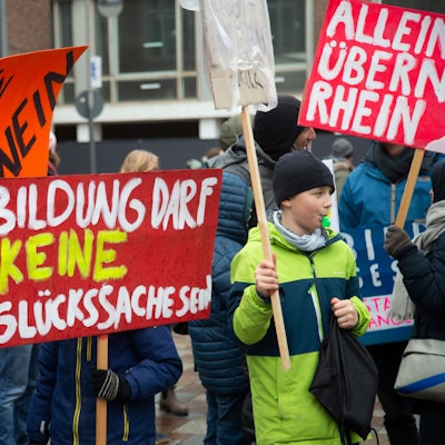 Man sieht Kinder mit Plakaten, die die Schulpolitik kritisieren.