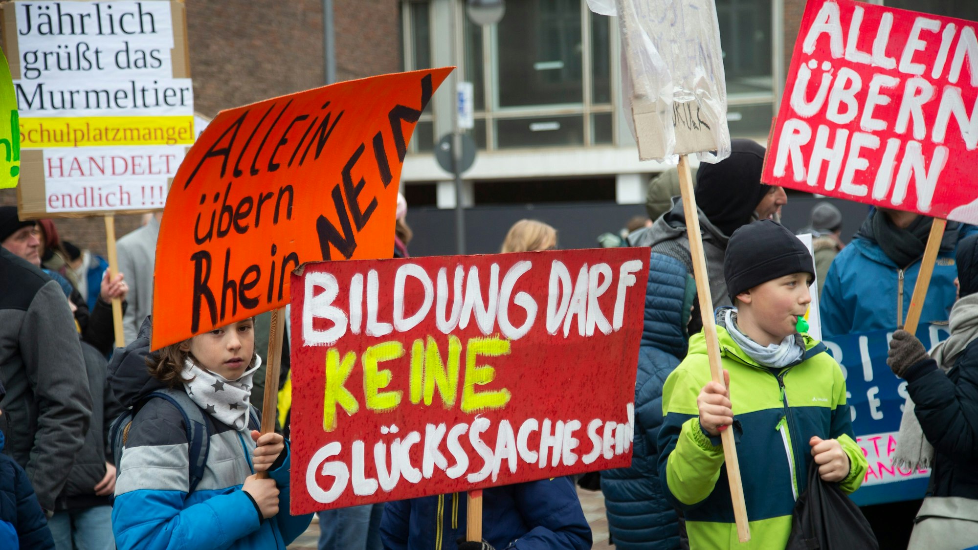 Man sieht Kinder mit Plakaten, die die Schulpolitik kritisieren.