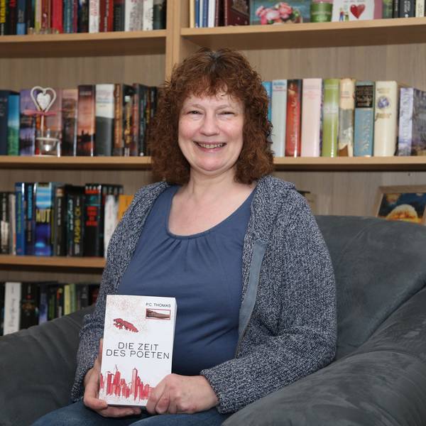 Eine Frau hält lächelnd ein Buch mit dem Titel „Die Zeit des Poeten“ in den Händen.
