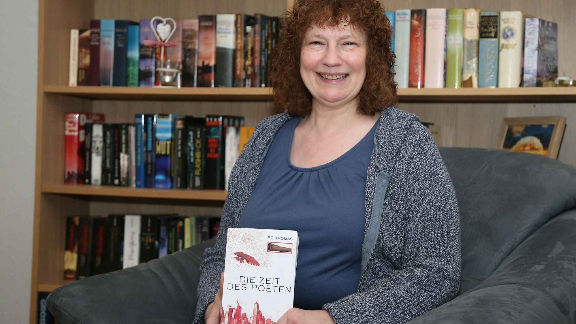 Eine Frau hält lächelnd ein Buch mit dem Titel „Die Zeit des Poeten“ in den Händen.