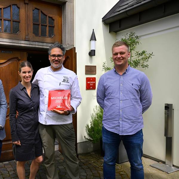 Michael und Birgitta Quendler stehen vor ihrem Restaurant und halten die Auszeichnung des Guide Michelin von 2022, eine rote Plakette.