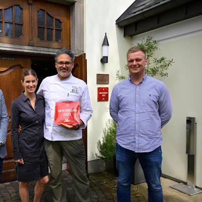 Michael und Birgitta Quendler stehen vor ihrem Restaurant und halten die Auszeichnung des Guide Michelin von 2022, eine rote Plakette.