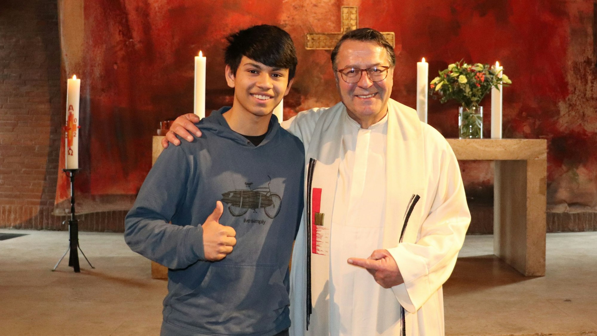 Die beiden stehen vor dem Altar. Hinter dem Altar hängt ein großes rötliches Tuch.