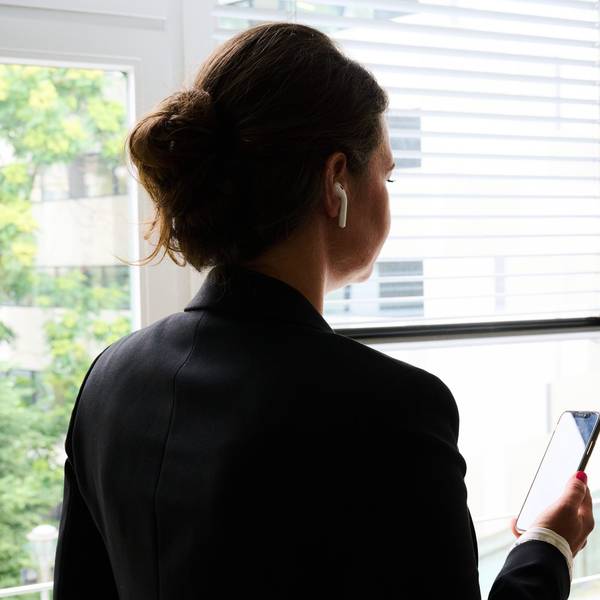 Eine Frau steht in einem Bürozimmer am Fenster und telefoniert über ein Headset. (gestellte Szene)