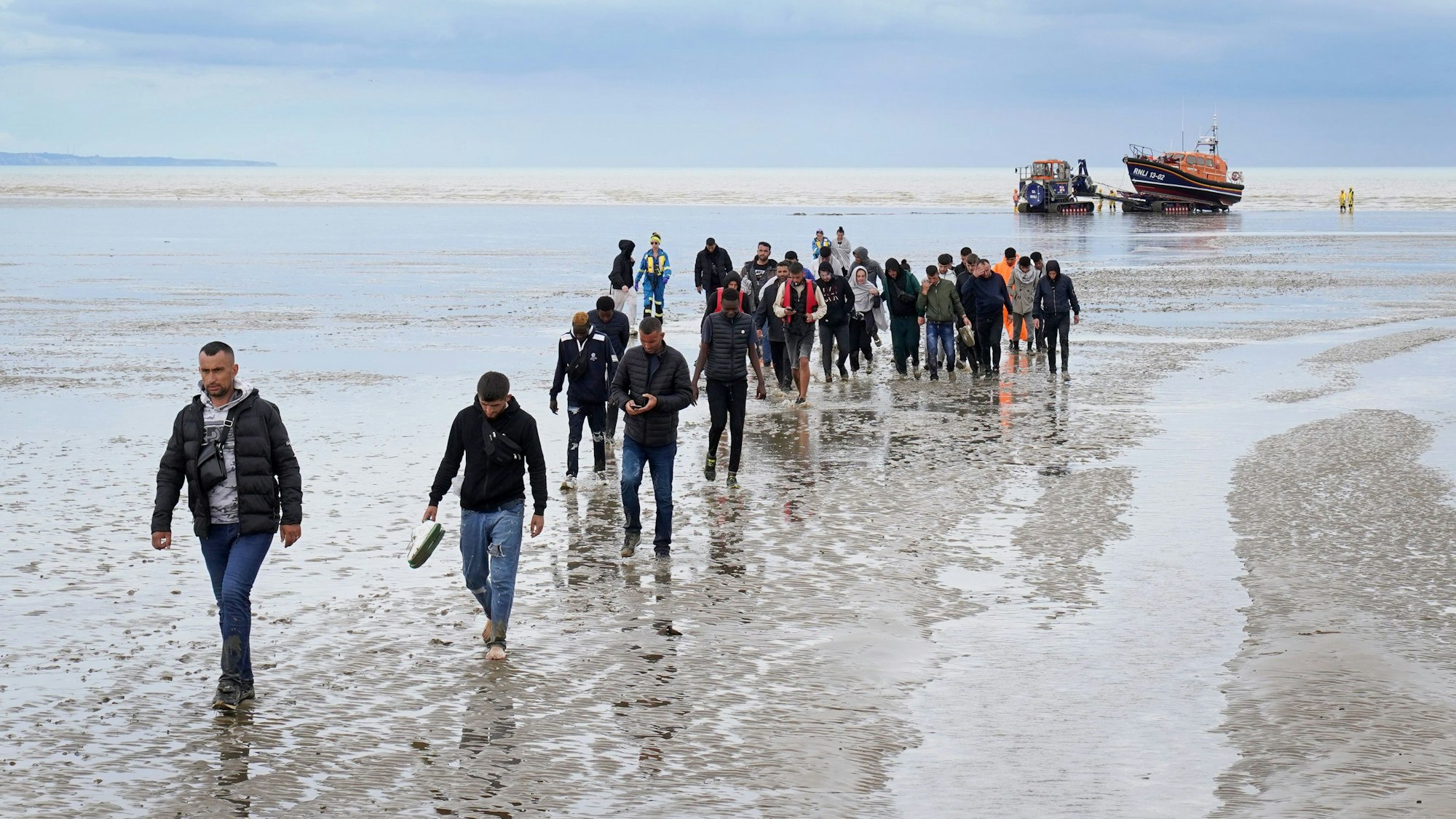 Eine Gruppe von Menschen, bei denen es sich vermutlich um Migranten handelt, geht an Land, nachdem sie nach einem Zwischenfall mit einem kleinen Boot im Ärmelkanal vom Rettungsboot ‚Dungeness‘ abgefangen wurde.