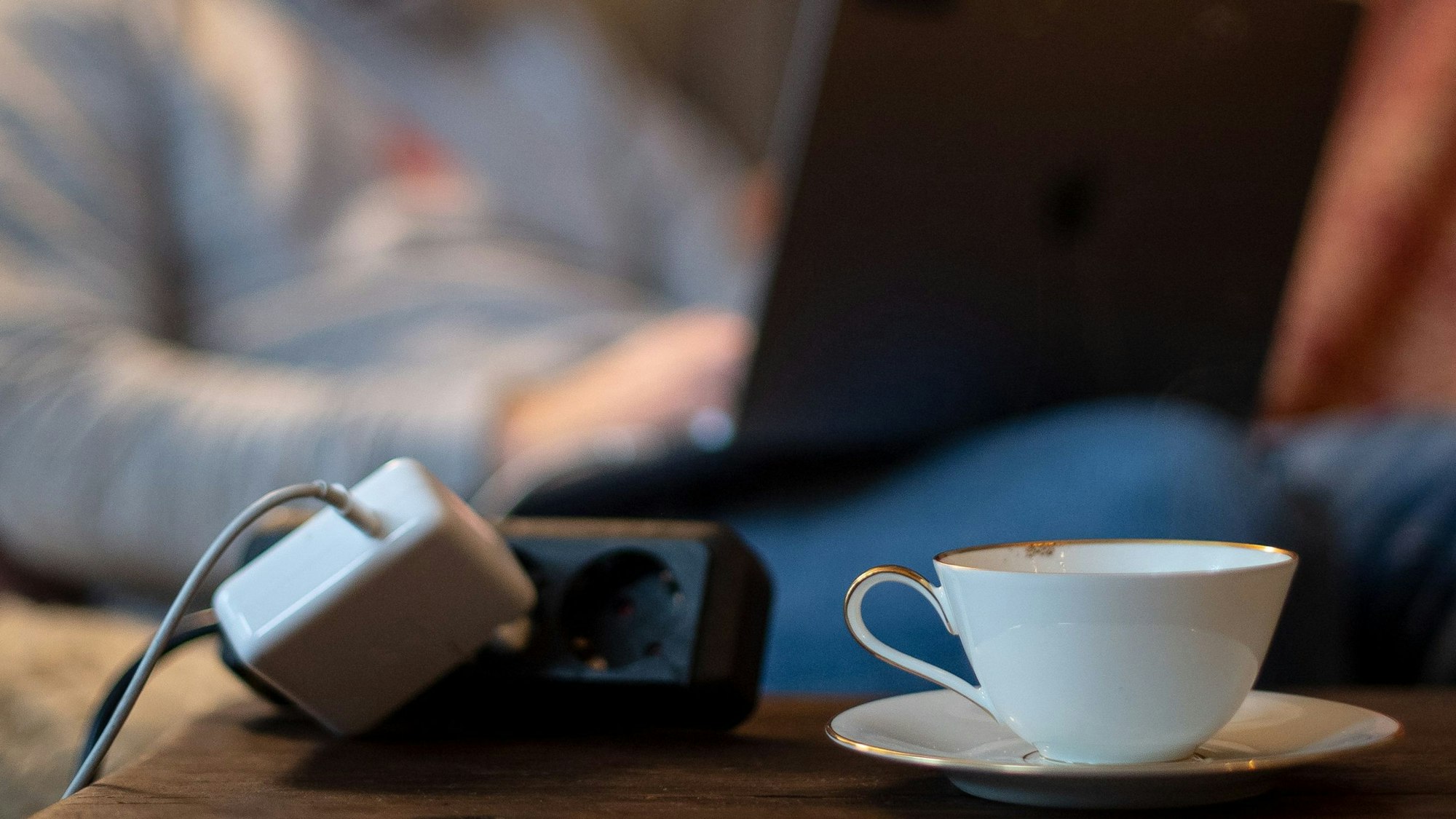 Ein Mann sitzt mit Laptop auf dem Sofa und macht seine Steuererklärung, vor ihm steht eine Tasse Tee.