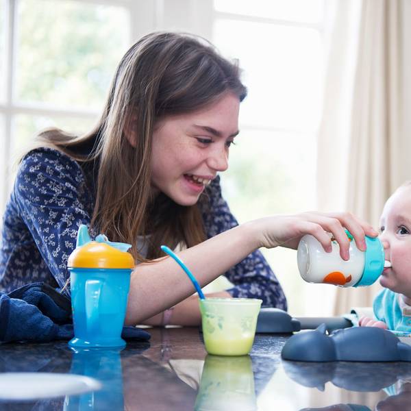 Ein Mädchen gibt einem Baby am Tisch eine Flasche.