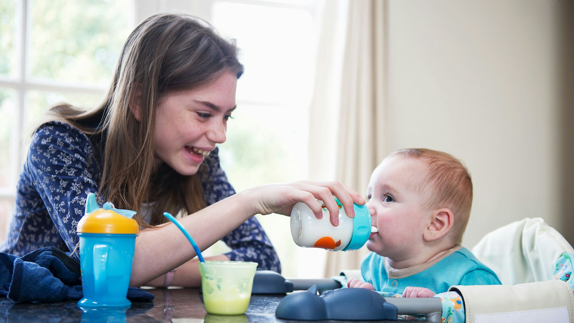 Ein Mädchen gibt einem Baby am Tisch eine Flasche.
