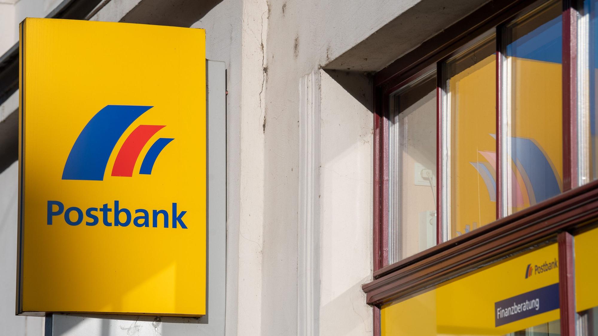Ein Schild mit dem Logo der Postbank ist an der Fassade einer Bankfiliale angebracht.