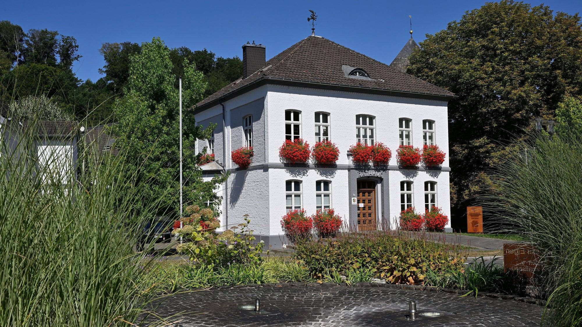 Rathaus Odenthal mit roten Geranien vor den Fenstern, vor dem Haus ein Springbrunnen